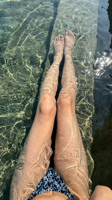 A person's legs visible in clear, shallow turquoise water with sunlight rippling across the surface.