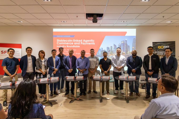 Group photo of approximately 14 people standing in a row at an industry roundtable event, with a projection screen behind them reading 'Stablecoin-linked Agentic Commerce and Payments - Industry Roundtable'.