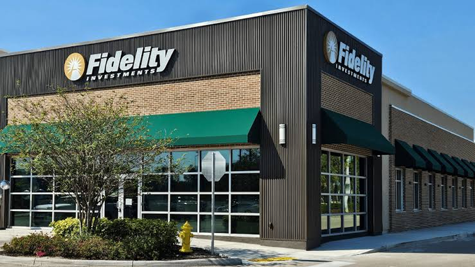 The image shows a Fidelity Investments branch building featuring the company's logo prominently displayed on dark paneled walls above green-striped awnings, with large glass windows and a small landscaped area including a yellow fire hydrant in front. The building serves as a visual representation of Fidelity, the asset management company filing the SEC proposal to add staking capabilities to its Ethereum ETF fund FETH.