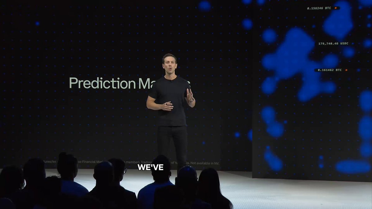 In this image, a man is standing on stage addressing an audience of people who are also present at the event. The speaker appears to be talking about cryptocurrency trading strategies or predicting future prices for various virtual assets like Bitcoin (BTC), Etherium (ETH), Litecoin (LTC), Ripple (XRP), and more. The setting seems to be a large conference room with a presentation screen behind the speaker, which displays an advertisement for Coinbase, a cryptocurrency exchange platform.