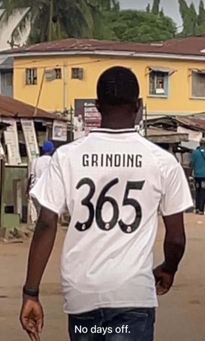 A person viewed from behind wearing a white jersey with 'GRINDING 365' printed on the back, walking down a street with the caption 'No days off.'