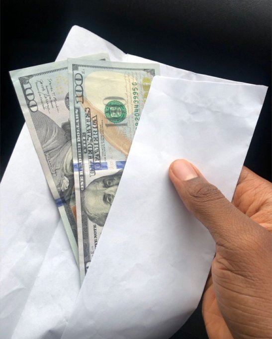 A hand pulls US $100 bills from a white envelope, with the serial number "L200439995C" visible, illustrating the message that money is a tangible key to security and freedom.