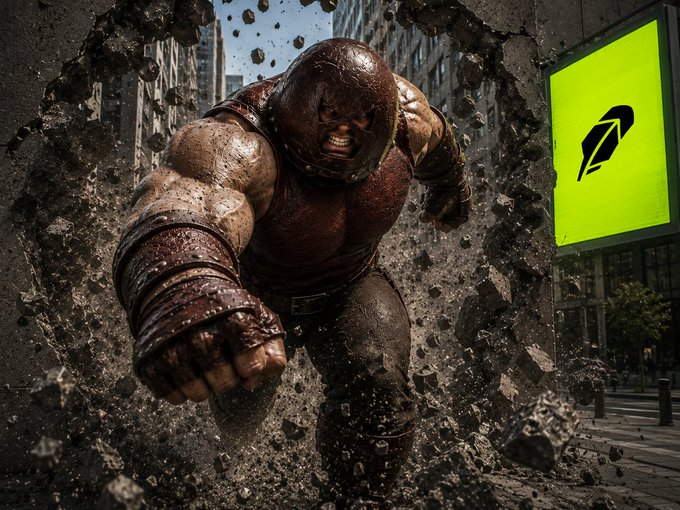 A massive, armored figure bursts through a concrete wall in an urban setting, with a green Robinhood logo visible on a building in the background, symbolizing the unstoppable $Juggernaut meme coin breaking into the Robinhood platform.