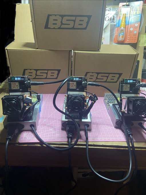 Three compact BSB (Block St Boys) mining units are displayed on a pink work mat, each equipped with cooling fans and control boards, with "BSB" branded boxes stacked behind them. The setup reflects the post's praise for the small but capable 1.8 TH/s miners running efficiently at 50°C, designed by NullHashrate for the Block St Boys team.