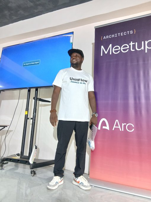 A man wearing a "UnitFlow - Finance on Arc" t-shirt and a black cap stands confidently at an Arc Architects Meetup event, with the purple Arc banner and a presentation screen displaying "No Signal or Weak Signal" visible behind him in Nsukka, Nigeria.