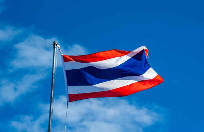 The Thai national flag waves against a bright blue sky, visually anchoring a post about Thailand's SEC proposing new rules to allow retail investors access to regulated overseas crypto derivatives. The flag serves as a national symbol linking the regulatory developments directly to Thailand's financial landscape.