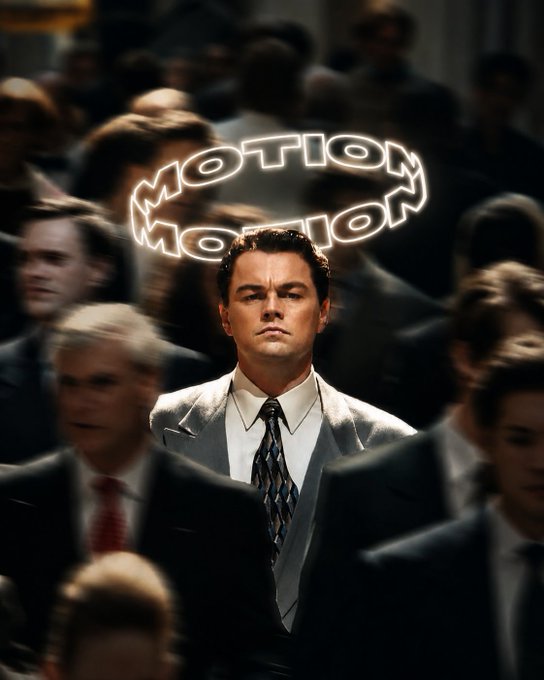 A man in a gray suit stands still amid a crowd of blurred, rushing businessmen, with a glowing neon-style sign reading "MOTION MOTION" hovering above his head—visually reinforcing the post's message "Be the $MOTION you want to see" by contrasting his stillness against the chaotic motion surrounding him.