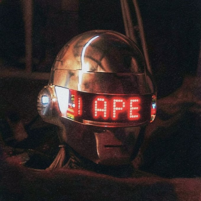 A metallic robotic helmet glows with red LED text reading "APE" on its visor, its chrome surface reflecting the dim ambient light. The "APE" display ties into the post's "You know the deal..." caption, likely referencing the ape-themed token or project the helmet represents.