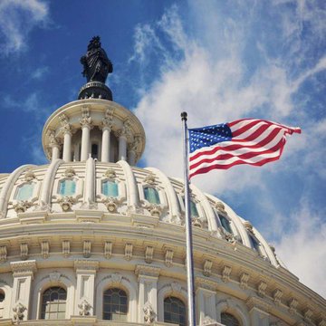 The U.S. Capitol building dome with an American flag waving in the foreground against a blue sky.