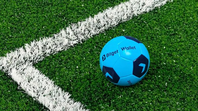 A blue soccer ball branded with "Bitget Wallet" rests on artificial turf near a white boundary line. The image ties into the post's "GMGM" message by using the ball as a metaphor for kicking off a trading strategy with Bitget Wallet as the tool to score in the crypto market.