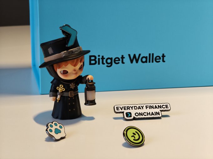 A Bitget Wallet branded figurine dressed as a wizard, holding a lantern, is displayed alongside a "EVERYDAY FINANCE ONCHAIN" tagline with paw and coin-shaped logos, presented on a blue background. The image showcases the promotional gift from Bitget Wallet mentioned in the post, highlighting the brand's merchandise quality as the recipient transitions to learning tennis.