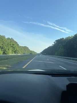 The image shows a car's windshield with a view of an empty highway, surrounded by trees. There are no other cars visible in the photo. The text "GM Raleigh bound Bored Ape Yacht Club" appears near the bottom right corner of the image. This suggests that the car might be on its way to or from a nearby event or gathering at the GM Raleigh bound Bored Ape Yacht Club, which could explain why there are no other cars visible in the photo.

The scene is captured through the windshield of a car, providing an inside perspective of the journey. The driver's view shows that they are driving on the highway and looking towards the horizon where trees can be seen lining the road.