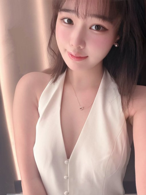 The image features a young woman wearing a white dress with a halter neckline, posing for a photo. She has dark hair and is smiling at the camera. The background of the image appears to be a room or a hallway, providing context about where she might be taking this picture. The caption accompanying the image reads: "宝宝们今天素我生日(*≧ω≦) 可不可以留一句生日快乐捏～ 感谢榜一大哥 @chameleon_jeff 从新加坡空投的生日礼物 $HYPE to the moon ♪(ε｀ )."