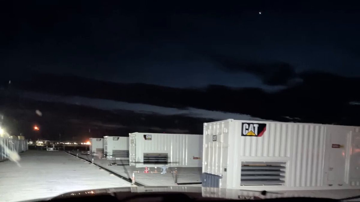 The image shows a row of white buildings with "Cat" written on them, likely representing a storage facility or warehouse. There are several large white containers lined up next to each other, indicating that they might be used for storing goods or equipment. The scene is set against a dark sky at night, which adds an element of mystery and intrigue to the image.