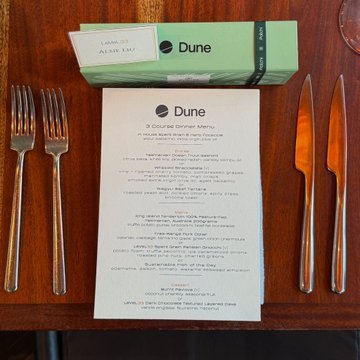 A 3-course dinner menu from Dune sits on a wooden table set with forks and knives, including a "Hapagari Eggplant" dish on a green Dune-branded card. The setup reflects a professional business dinner in Singapore, fitting the post about the Dune institutional team's meetings with APAC partners.