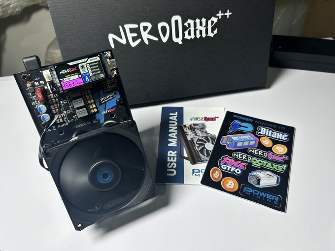 A NerdQaxe++ crypto mining device displayed with its components including a cooling fan, circuit board, user manual, and a sticker sheet featuring logos for Bitaxe, Power 3, NerdMiner, and Bitcoin.
