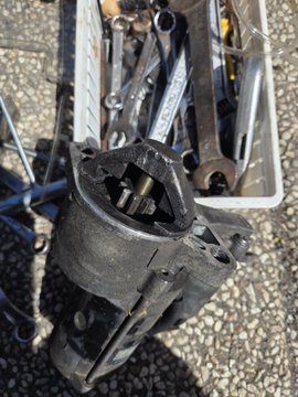A disassembled mechanical component or engine part resting on a tiled floor with tools nearby.