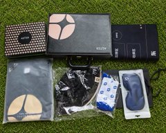 An assorted collection of small packaged items, boxes, and accessories scattered on a grassy surface, including a polka-dot box and various branded packages.