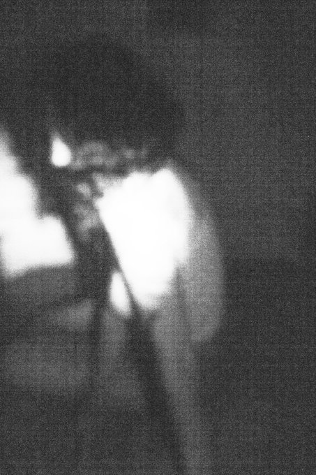 A blurry, grainy black and white photo showing an unidentifiable person with a bright white area obscuring the right side of their face, creating a mysterious atmosphere.