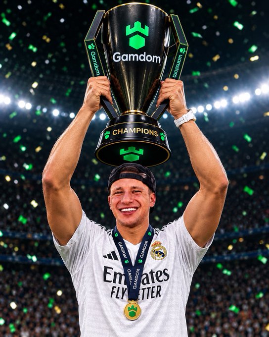 A Real Madrid player wearing a white jersey holding a black 'Gamdom' Champions trophy with a gold medal, celebrating with confetti in the background.