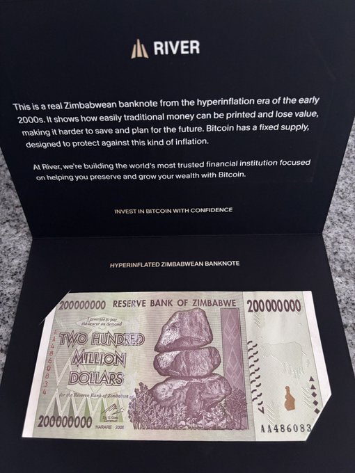 A River-branded display showcasing a real Zimbabwean 200,000,000 (200 million) dollar hyperinflation-era banknote, with text explaining how fiat currency loses value and positioning Bitcoin's fixed supply as a hedge against inflation. The display reinforces the post's message about protecting and growing purchasing power over time through assets like Bitcoin.
