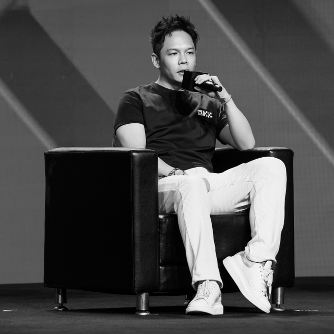 A man in a black t-shirt and white pants sits in a black armchair on stage, speaking into a microphone while discussing X Layer's programmable infrastructure at Bitcoin Asia.