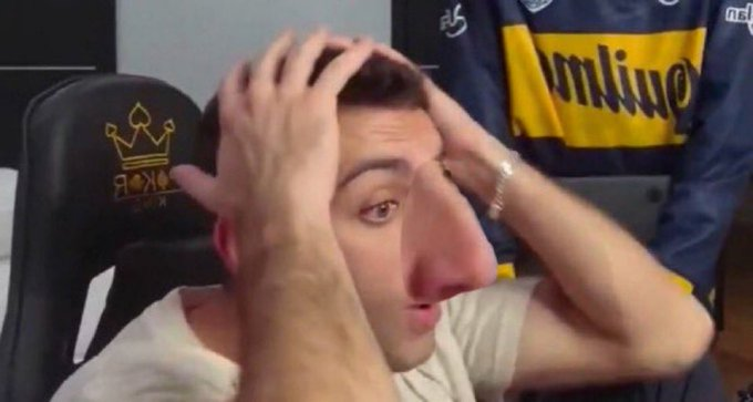 A man with a comically distorted, large nose sitting in a gaming chair, holding his head in his hands in apparent frustration.