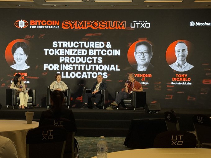 Photo from the Bitcoin Symposium for Corporations, presented by UTXO, showing a panel discussion titled 'STRUCTURED & TOKENIZED BITCOIN PRODUCTS FOR INSTITUTIONAL ALLOCATORS' with speakers including Yehong Ji (Babylon), Tony DiCarlo (Rootstock Labs), and moderator Junfei Ren.