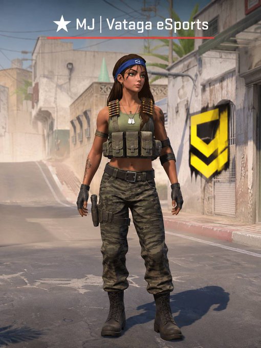 A video game character in military-style camouflage pants and a tactical vest stands in an urban setting; the image is labeled "MJ | Vataga eSports" at the top and features a yellow chevron logo on a wall.