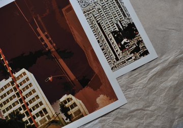 Two prints lie on a textured beige fabric surface, featuring dark, monochromatic architectural imagery of the Golden Gate Bridge and a cityscape in deep burgundy and black tones. The post promotes signed limited-edition prints from the "Buidlings" collection on Ordinals, with the artwork showcasing the same dramatic, stylized urban and landmark subjects highlighted in the collection.