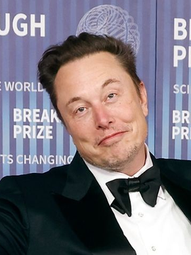 Elon Musk smiles at the 10th Breakthrough Prize ceremony, with backdrop text reading "BREAKTHROUGH PRIZE" partially visible behind him. The image ties to news that his companies—Tesla and SpaceX—are holding approximately $1.35B in unrealized Bitcoin gains.