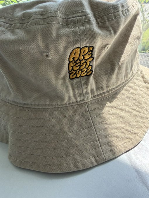 A tan bucket hat featuring an embroidered patch that reads 'APE FEST 2023' in yellow and black lettering.
