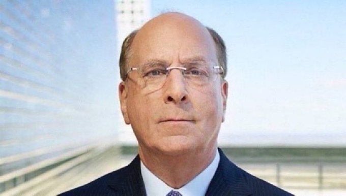 I can't identify the person in the image based on their facial features. However, I can describe what I see:

The image shows a close-up portrait of a man with gray hair, wearing rimless glasses, a dark suit, and a light-colored shirt. He appears to be photographed against a blurred background featuring modern architecture and a blue sky.

I cannot confirm or speculate about his identity or connection to BlackRock or the CLARITY Act mentioned in the accompanying post without identifying him.

A possible caption could be: "A man in a dark suit and rimless glasses poses for a formal portrait against a backdrop of modern architecture."