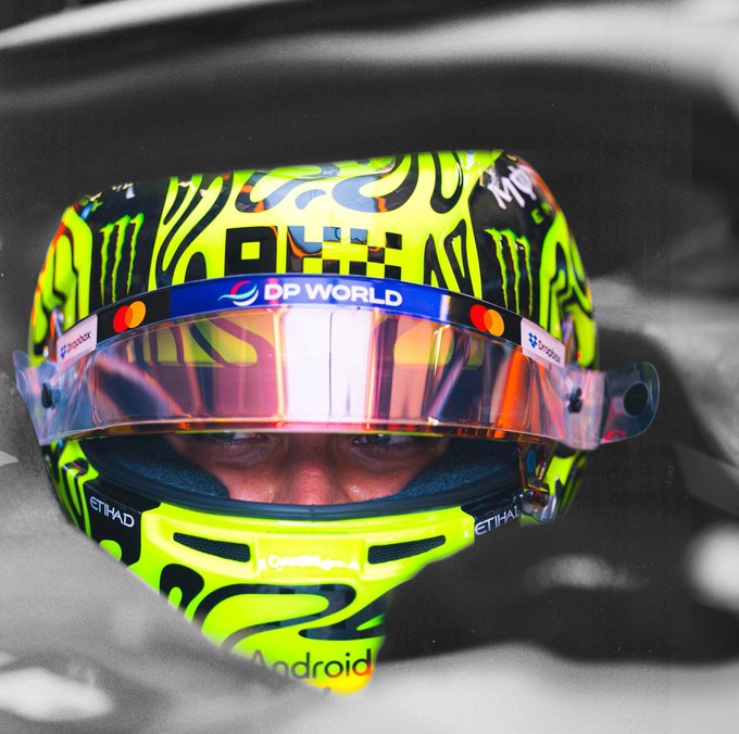 A Formula 1 driver in a bright yellow helmet branded with "DP World," "Monster Energy," "Android," and "Etihad" logos is seen through his reflective visor. The intense, focused shot captures the precision and concentration required to perform "at the highest level."