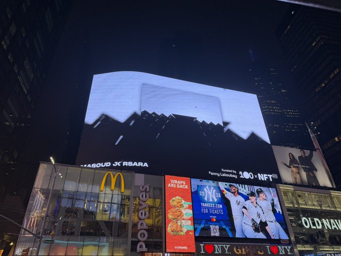 A nighttime view of a large billboard in Times Square displaying a piece of digital art, with visible advertisements below for McDonald's, 'Wraps Are Back', Yankees tickets, and Old Navy.