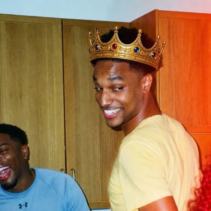 A man wearing a golden jeweled crown smiles at the camera while another person laughs in the background, playfully embodying the "king" role suggested by the post's message about commitment and focus, with the caption "those who commit to nothing are distracted by everything! committed to $ansem" reinforcing the royal/commitment theme.