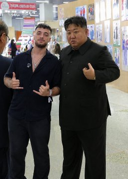 A man in a black polo shirt poses next to a man resembling Kim Jong Un, both making hand gestures, in what appears to be a convention or exhibition hall. The image suggests it is meant to display Kim Jong Un's fitness, though the setting and casual attire appear inconsistent with typical North Korean media releases.