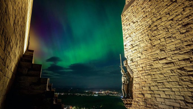 A stone monument with a soldier statue stands illuminated against a vibrant green and purple aurora borealis in the night sky, overlooking distant city lights from a hilltop. The serene nighttime scene with its natural light display loosely mirrors the post's theme of restful sleep and tranquility.