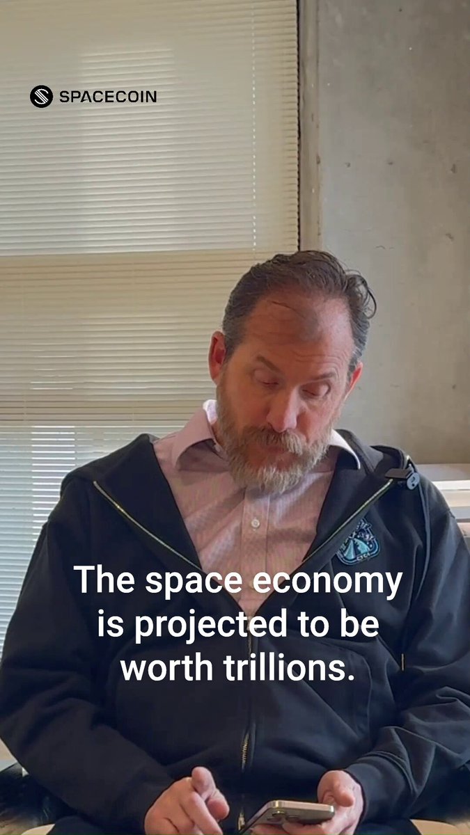 The image features a man sitting down, looking at his cell phone while wearing a black jacket. The background of the image shows a window that has blinds covering it. There are also some text elements present in the image, including "Space economy is projected to be worth trillions." and "Building crazy things is one thing. Building crazy things that are actually useful in the real world is another. Crypto has struggled with the latter. (you know it too) Space is a use case that you didn't know was possible with blockchain tech. Let'S open it up to everyone."