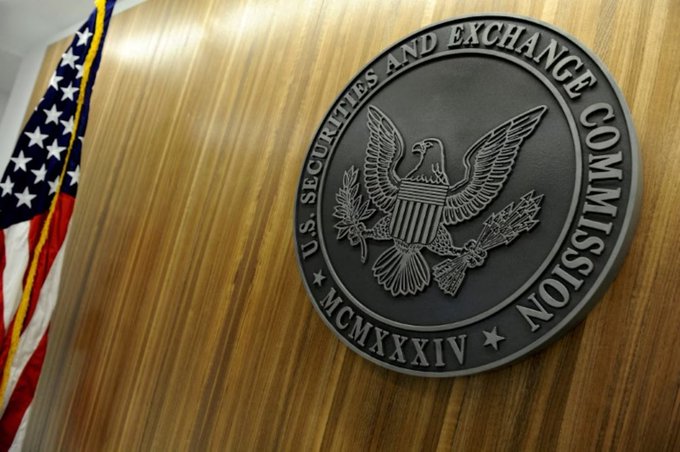 A photograph of the U.S. Securities and Exchange Commission (SEC) seal mounted on a wooden surface, featuring an eagle with a shield, olive branch, and arrows, with an American flag visible on the left side.