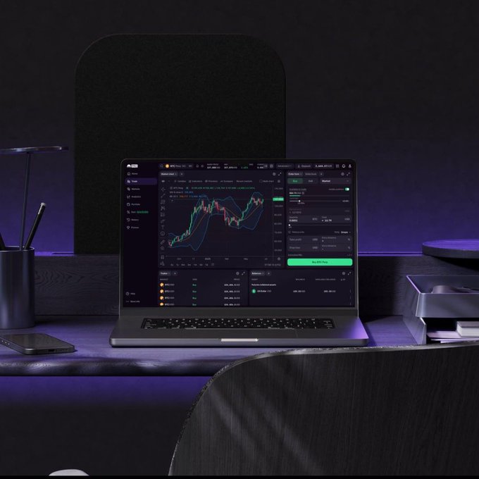 A laptop on a dark desk displaying a cryptocurrency trading chart interface, with purple ambient lighting and a modern workspace setup.