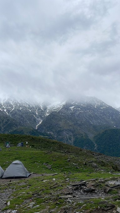 The image shows a beautiful mountain landscape, featuring a green field with tents pitched at various locations. The sky above appears cloudy, creating an atmospheric backdrop for the scene. In the background, there are mountains covered in snow, adding to the picturesque view. The text "Good morning homies @NomismaNetwork is refining its value coordination layer with more adaptive liquidity flow and distribution logic that reacts dynamically to live ecosystem activity instead of static allocation cycles @River4fun is continuing to improve its reward engine" suggests a connection between the camping area and the ongoing efforts in the cryptocurrency world. The image captures the essence of both natural beauty and technological advancements, creating an interesting juxtaposition for viewers.