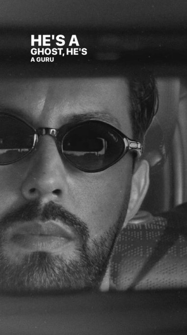A black-and-white close-up of a bearded man wearing dark sunglasses, with the stylized white text 'HE'S A GHOST, HE'S A GURU' overlaid on the image.