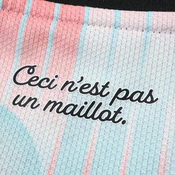 A close-up of a pink and blue striped athletic fabric printed with the black cursive text 'Ceci n'est pas un maillot.'