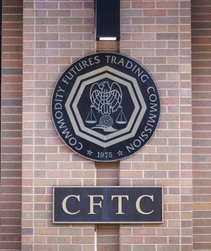 A circular seal for the Commodity Futures Trading Commission (CFTC) hangs on a brick wall above a plaque reading "CFTC" and "1975," representing the agency's authority to regulate cryptocurrency markets independently if the CLARITY Act fails to pass Congress.