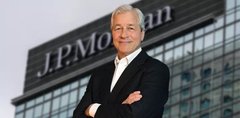 The image features a man dressed in a suit standing next to a building with a large J.P. Morgan sign above him, indicating that he might be associated with or working for the bank. The man has his arms crossed over his chest, giving off an air of confidence and authority. In the background, there is another person partially visible on the right side of the image.