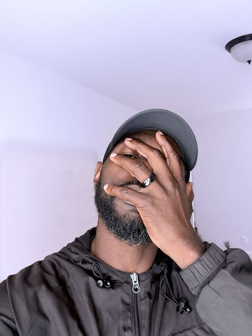 A man wearing a cap and jacket covering his face with his hand in what appears to be a facepalm gesture.