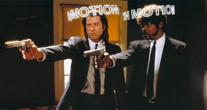 A still from the movie Pulp Fiction showing two men in black suits pointing silver handguns, with the 'In Motion' sign reflecting in the mirror behind them.