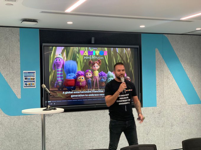 A man in a black t-shirt speaks into a microphone during a presentation about 'Zig & Sharko', described on screen as 'A global entertainment franchise that brings generations to embrace new adventures'.