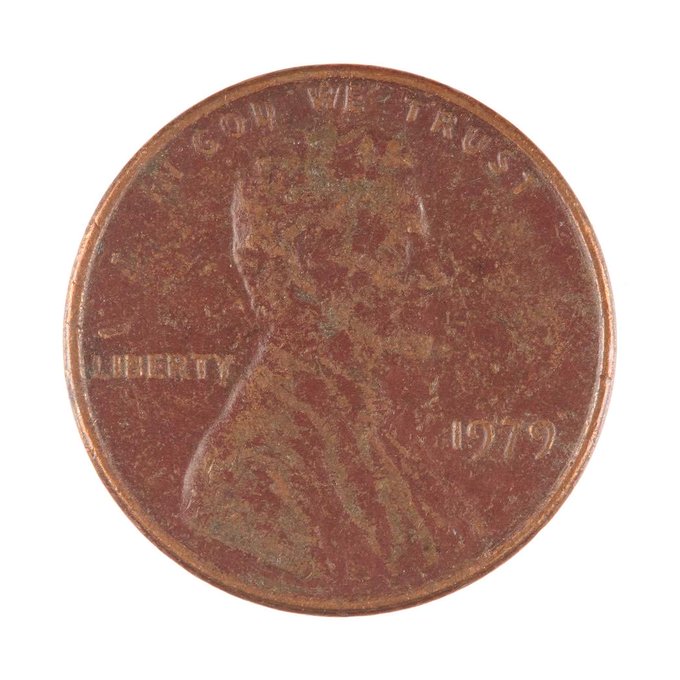 An extremely worn and corroded 1979 Lincoln penny showing 'IN GOD WE TRUST' and 'LIBERTY', with the portrait details almost completely eroded away.